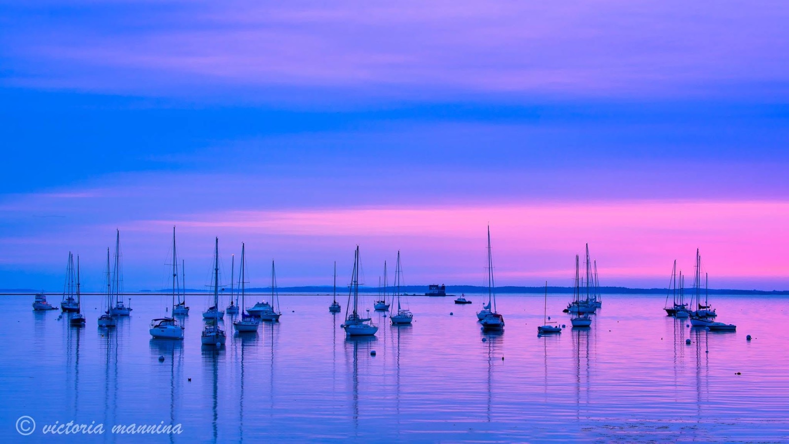 sailboats moored in calm harbor under a pink and purple sunset sky