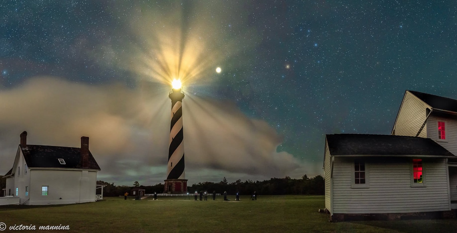 Lighthouse and keeper's houses under a starry sky with onlookers