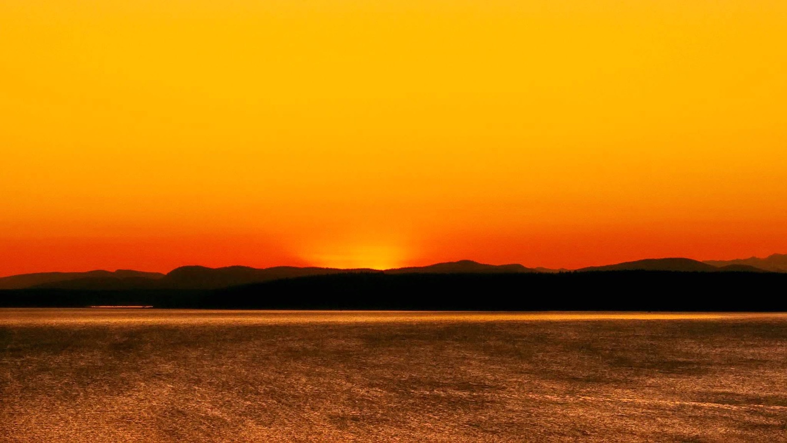 Fiery orange sunset sky over water and silhouetted shoreline