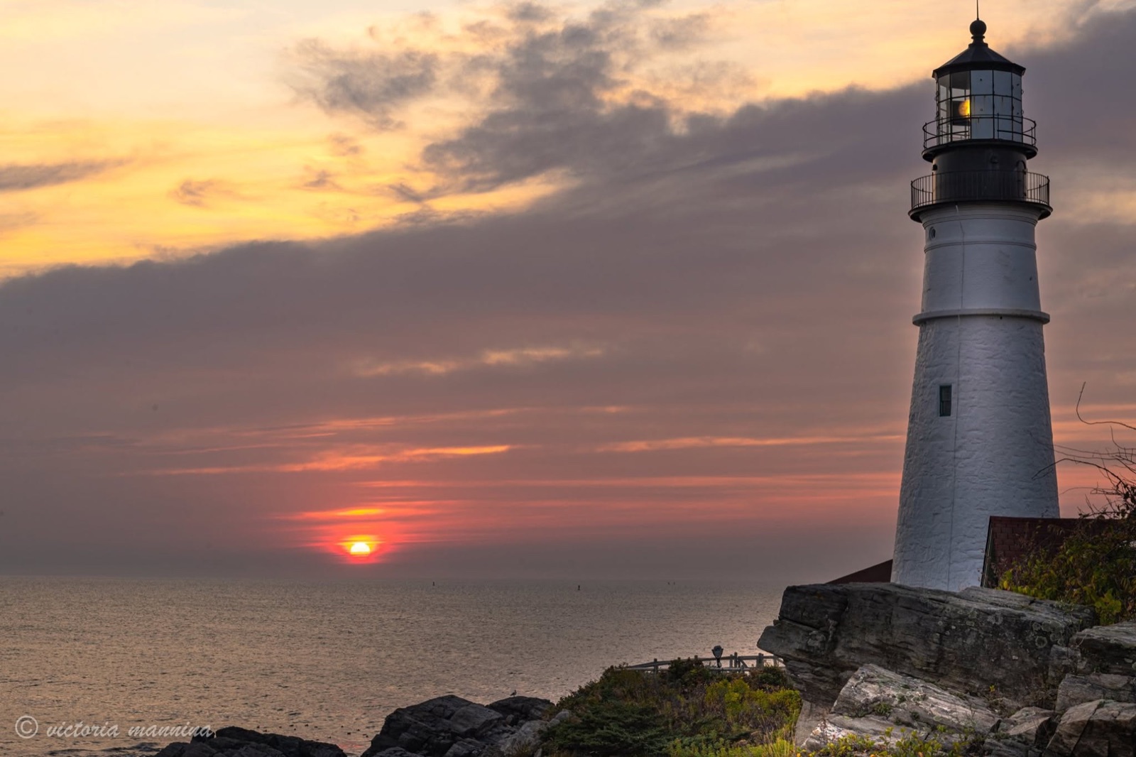 Lighthouse tower silhouetted against fiery sunrise